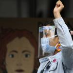 Woman in a face mask in the foreground with a raised fist. 