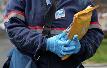 Postal worker holding a package wearing gloves.